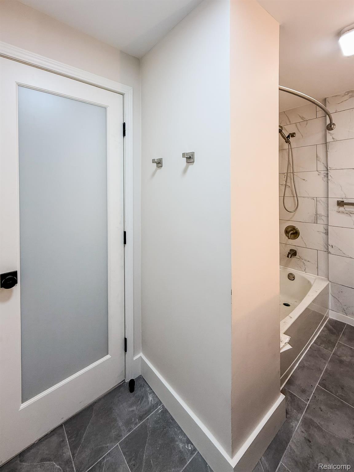 30052 Schoenherr Road Warren, MI 48088 - Photo 27 of 38 Bathroom featuring dark gray tile flooring, a white soaking tub with white subway tile surround, brushed nickel fixtures, and a white interior door with frosted glass panel