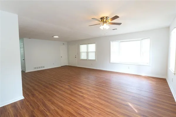 an empty room with wooden floor chandelier fan and windows