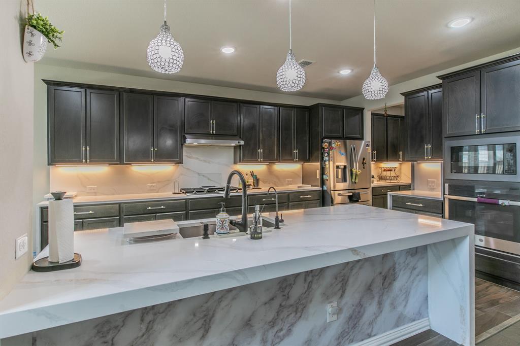 2521 Maidenhair Road Frisco, TX 75033 - Photo 6 of 39 Kitchen featuring a large island with waterfall-edge countertop, dark wood-finish cabinetry, stainless steel appliances, and crystal pendant lighting