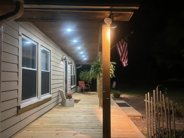 a view of a white house with a yard plants and lawn chairs with plants