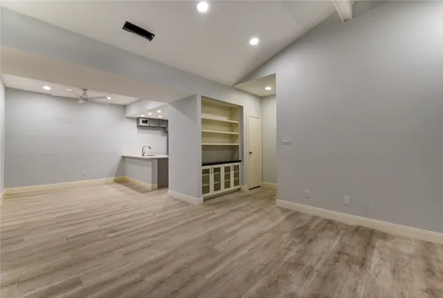 an empty room with wooden floor kitchen view and windows