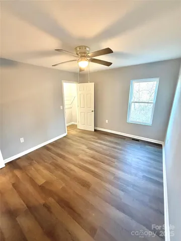an empty room with wooden floor chandelier fan and windows