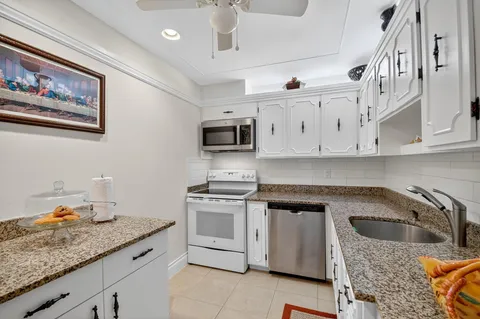 a kitchen with stainless steel appliances granite countertop a sink stove oven and white cabinets with wooden floor