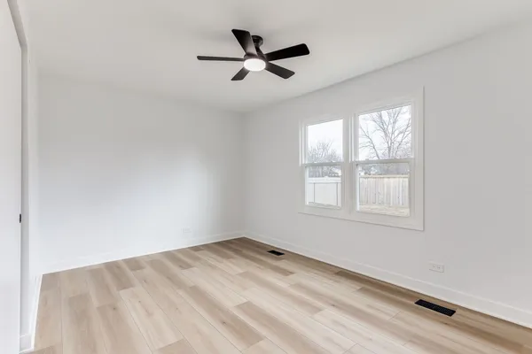 an empty room with wooden floor fan and windows