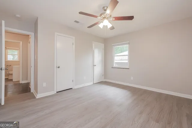 an empty room with wooden floor ceiling fan and windows