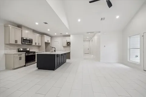 a large kitchen with stainless steel appliances granite countertop a stove a sink a refrigerator and white cabinets with wooden floor