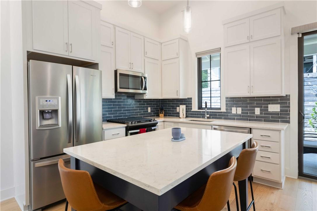 2002 East 9th Street, Unit 2 Austin, TX 78702 - Photo 8 of 32 A sleek island kitchen featuring crisp white cabinetry, durable countertops, and a modern blue subway tile backsplash.