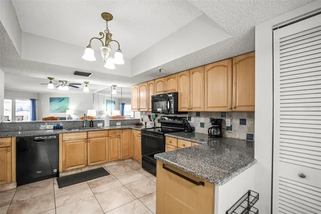 a kitchen with stainless steel appliances granite countertop a refrigerator a sink dishwasher a stove top oven a kitchen island and couches with wooden floor