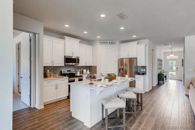 a kitchen with stainless steel appliances granite countertop a refrigerator oven a sink a stove a dining table and chairs with wooden floor