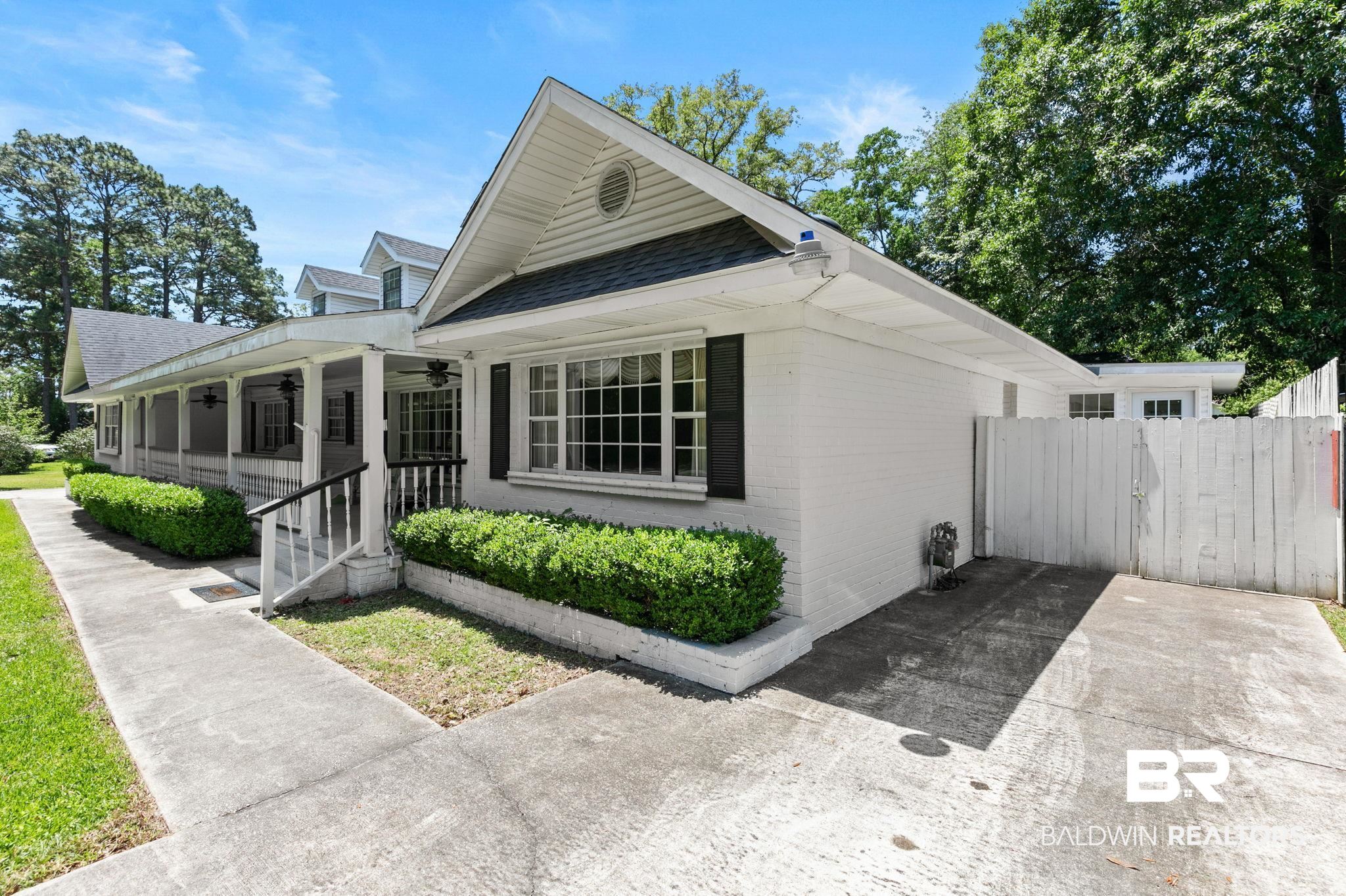 927 Cleveland Road Saraland, AL 36571 - Photo 76 of 80 White brick exterior featuring a covered porch, established shrubbery, dark window shutters, and a white privacy fence