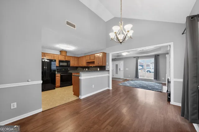 a view of an empty room and kitchen with wooden floor
