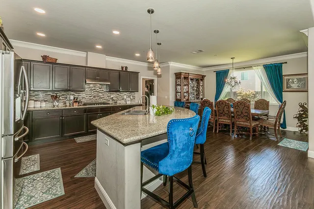 a kitchen with stainless steel appliances granite countertop a stove a refrigerator a kitchen island with chairs and wooden floor