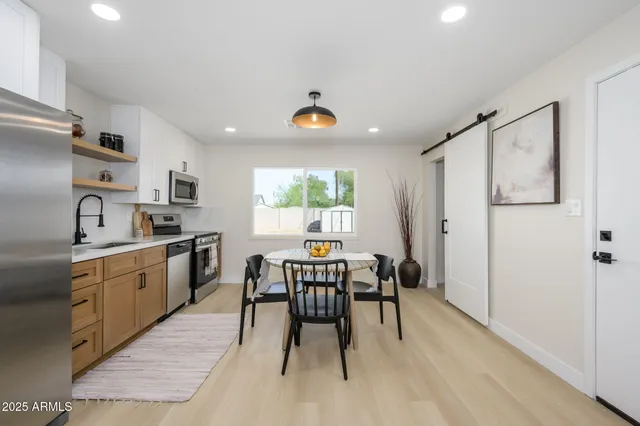 a kitchen with stainless steel appliances granite countertop a dining table chairs refrigerator and sink