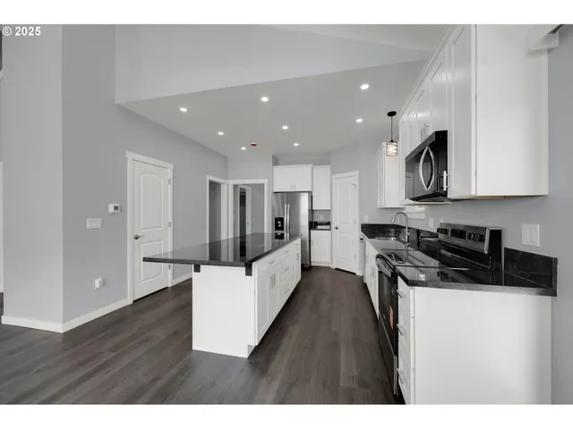 a kitchen with stainless steel appliances kitchen island granite countertop a stove a sink a refrigerator and white cabinets with wooden floor