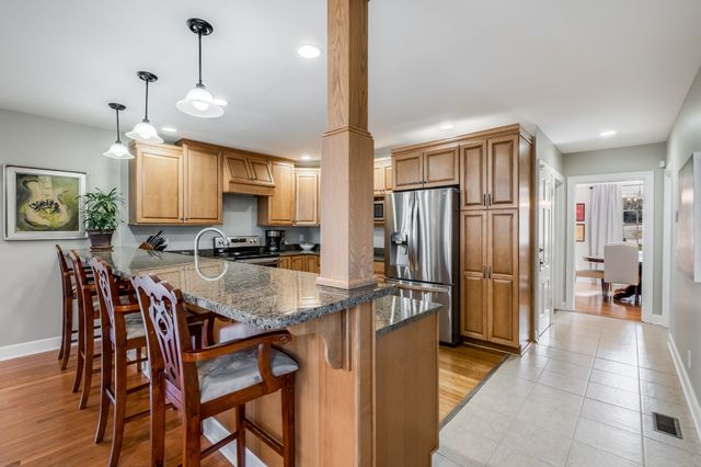 a kitchen with stainless steel appliances granite countertop a refrigerator a stove a sink a dining table and chairs with wooden floor