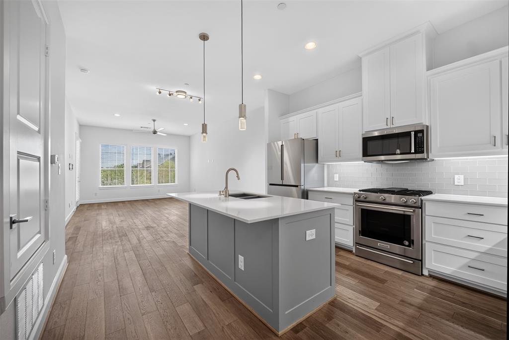5015 Meridian Lane, Unit 2102 Addison, TX 75001 - Photo 9 of 36 Open-concept kitchen and living area featuring stainless steel appliances, white shaker cabinetry, a subway tile backsplash, and wood-finish flooring