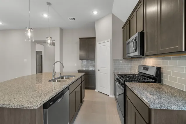 a kitchen with stainless steel appliances granite countertop a sink a stove and a wooden cabinets