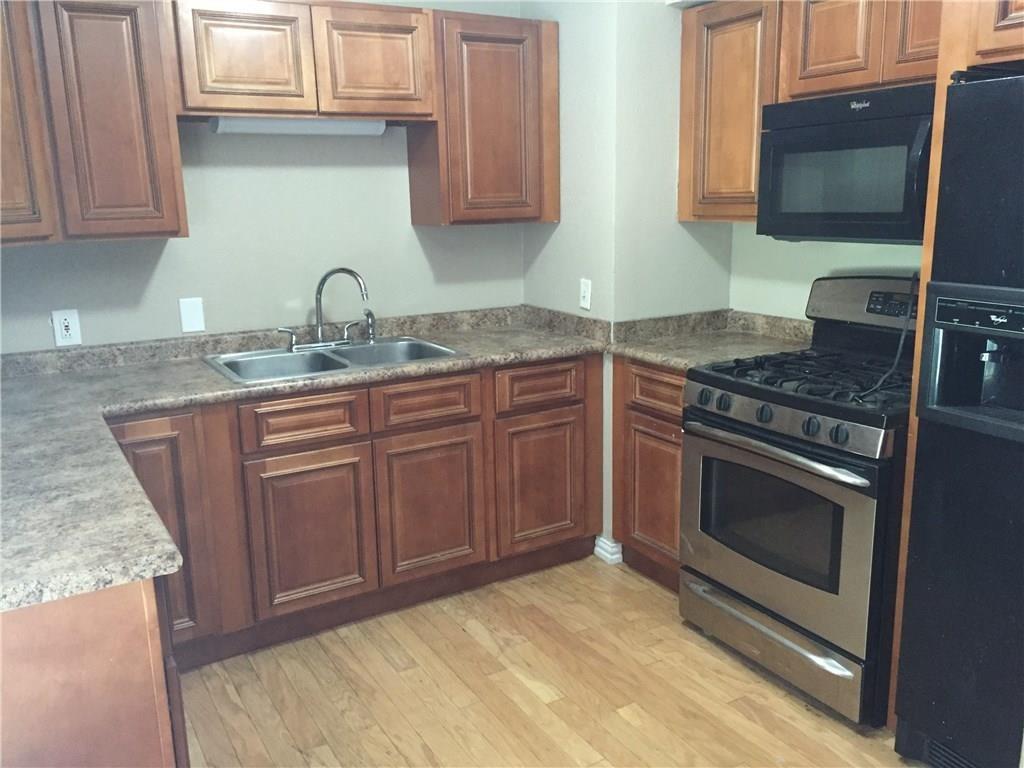 216 Elm Street Hurst, TX 76053 - Photo 11 of 17 Kitchen featuring wood-finish flooring, warm-toned cabinetry, laminate countertops, a double basin stainless steel sink, and stainless steel range