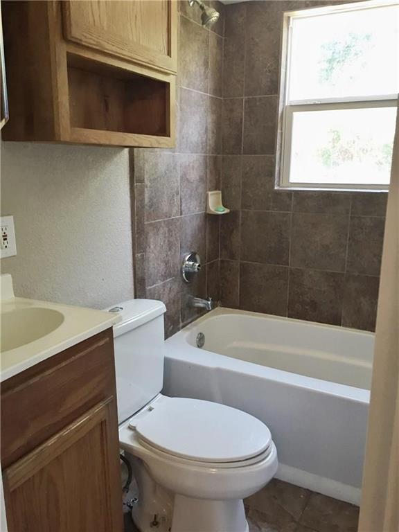 216 Elm Street Hurst, TX 76053 - Photo 15 of 17 Bathroom featuring a white bathtub, ceramic tile shower surround, window with natural light, wood-finish vanity with countertop and sink, and a white toilet