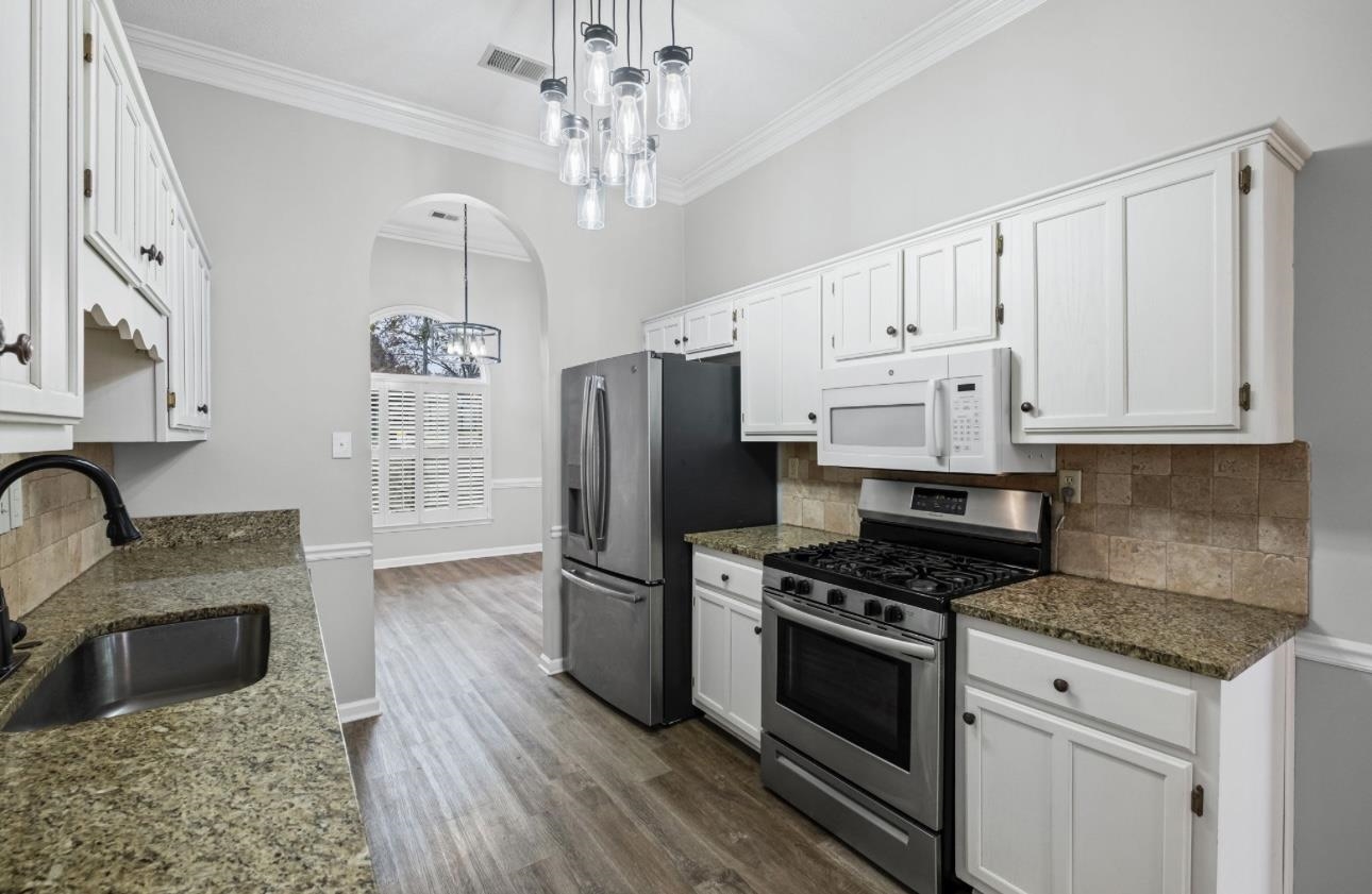 Kitchen with stainless steel appliances, crown molding, dark stone countertops, arched walkways, and pendant lighting