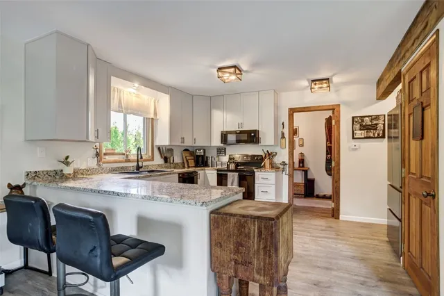 a kitchen with stainless steel appliances granite countertop a refrigerator a sink dishwasher a stove a dining table and chairs with wooden floor