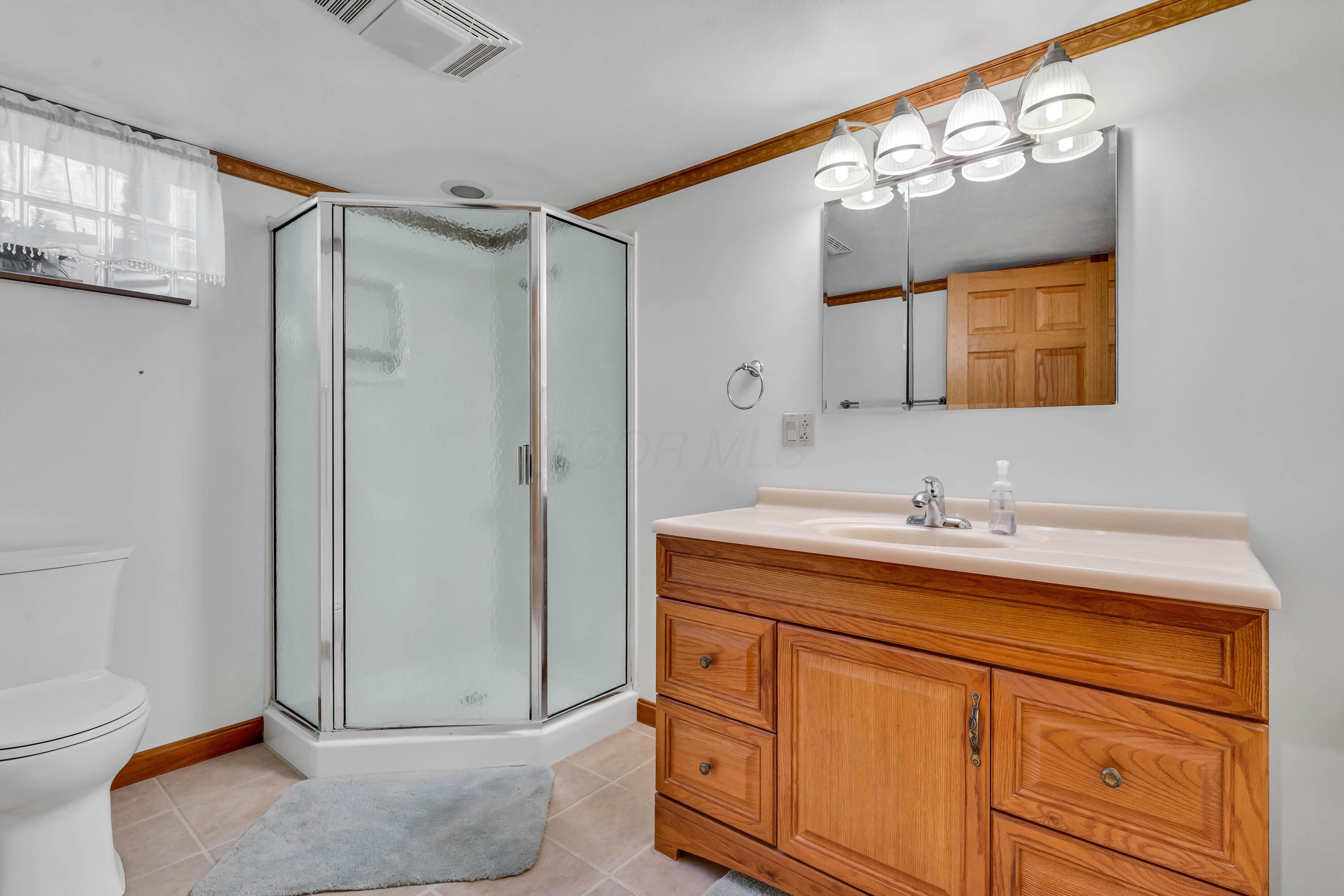 1213 East Cooke Road Columbus, OH 43224 - Photo 41 of 57 • Heated, ceramic tile flooring • Ivory painted walls • Crown molding • Lighted ceiling exhaust • Wall mirror • Shower stall with glass enclosure & cultured marble surround • Enclosed vanity with single bowl, cultured marble sinktop • 3 bulb wall light • Mirrored medicine cabinet