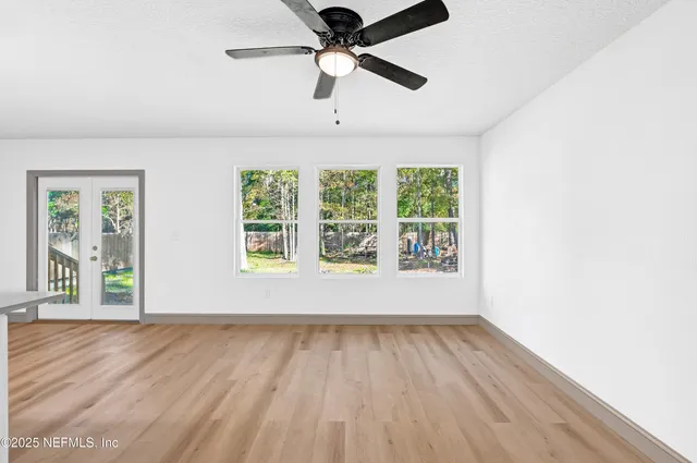 an empty room with wooden floor chandelier fan and windows