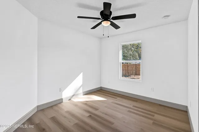 an empty room with wooden floor fan and windows