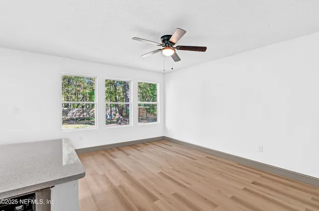 an empty room with wooden floor fan and windows