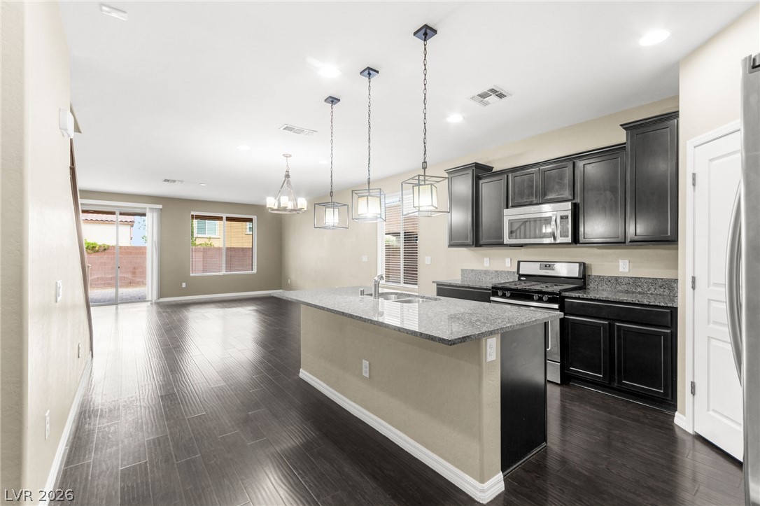 11048 Prairie Grove Road Las Vegas, NV 89179 - Photo 9 of 75 An open concept kitchen features sleek dark cabinetry, granite countertops, and modern pendant lighting over a central island.