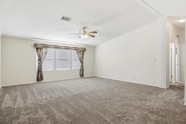 an empty room with chandelier fan and kitchen view