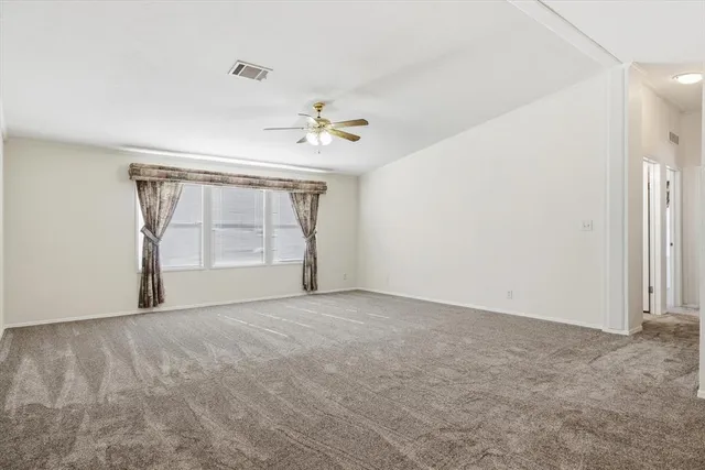an empty room with chandelier fan and kitchen view