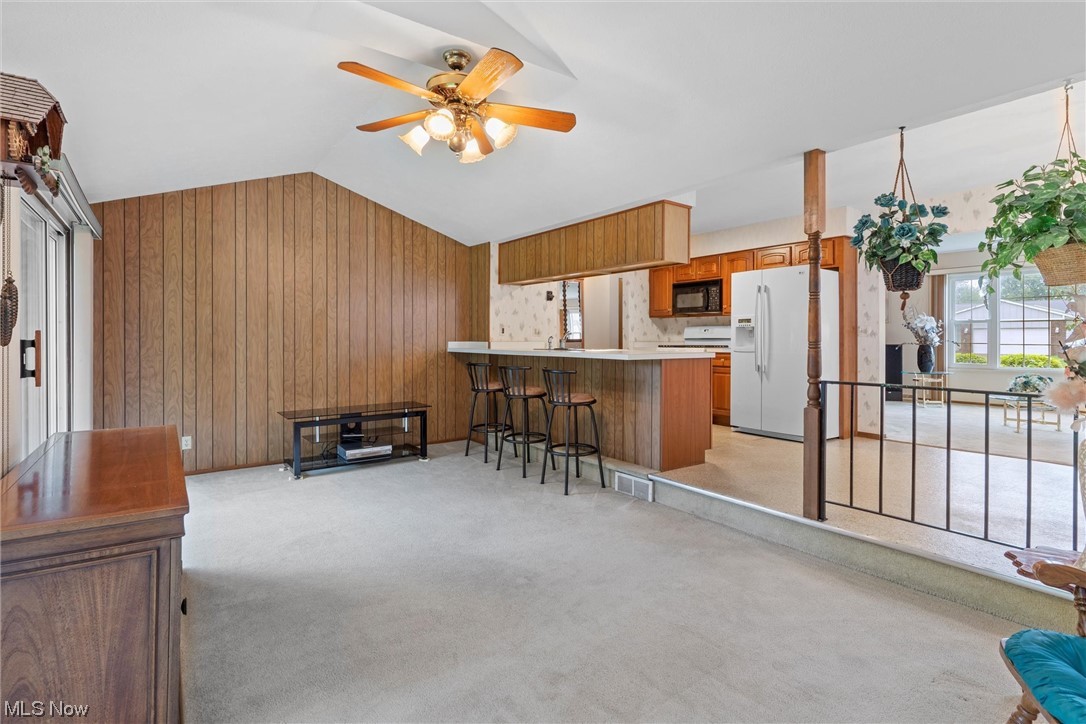 5624 Dolphin Road Mentor, OH 44060 - Photo 18 of 30 Kitchen featuring white fridge with ice dispenser, a kitchen island, lofted ceiling, wood walls, light carpet, brown cabinets, light countertops, and ceiling fan