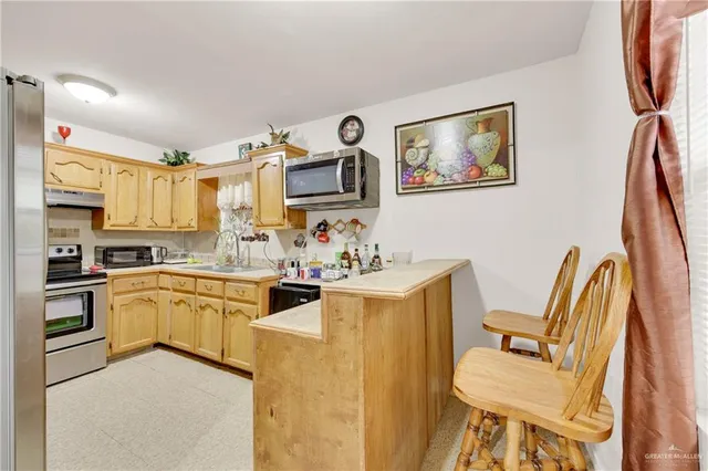 a living room with stainless steel appliances furniture a rug and a kitchen view