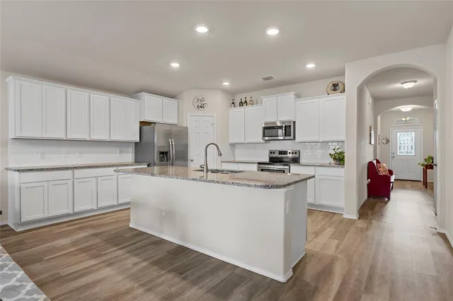 a kitchen with stainless steel appliances granite countertop a stove top oven a sink a refrigerator white cabinets and couches with wooden floor