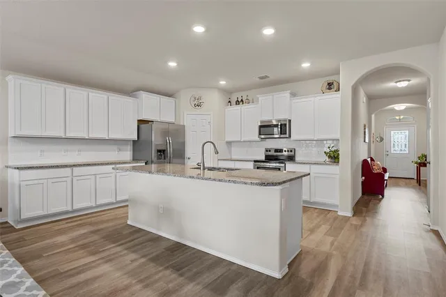 a kitchen with stainless steel appliances granite countertop a stove top oven a sink a refrigerator white cabinets and couches with wooden floor
