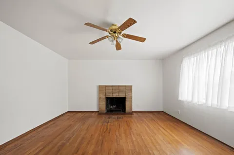 an empty room with wooden floor a ceiling fan and windows