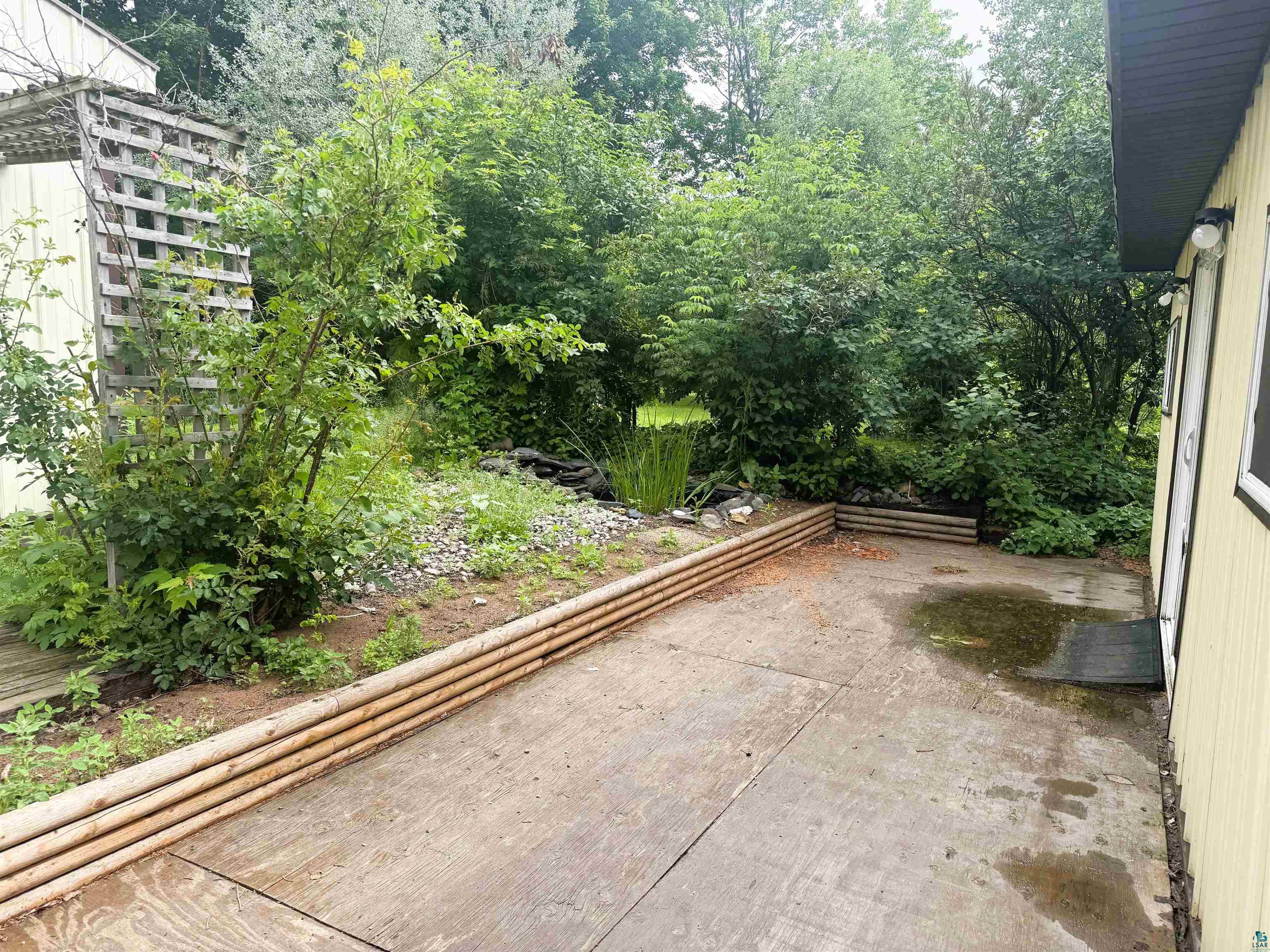 3541 Bent Trout Lake Road Barnum, MN 55707 - Photo 36 of 41 Rear exterior featuring a concrete patio, wood-finish retaining wall, mature trees, and a wooden trellis