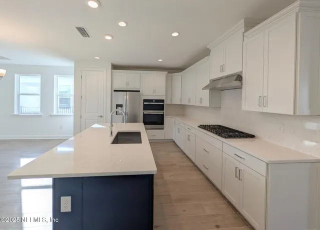 a large kitchen with stainless steel appliances a large counter top a stove a refrigerator a sink a center island and windows