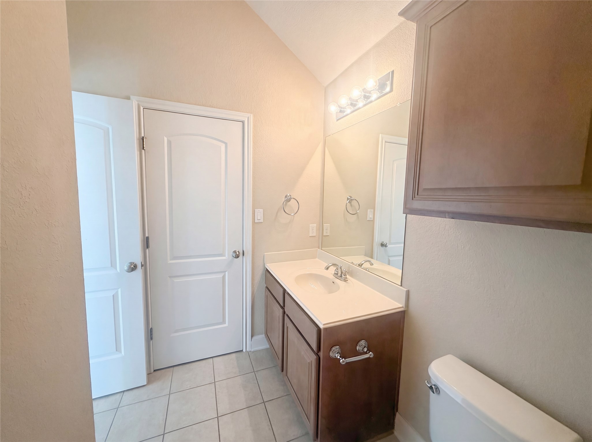104 Perpetuation Drive Austin, TX 78734 - Photo 17 of 29 Half bathroom with vanity, light tile patterned floors, lofted ceiling, and a textured wall
