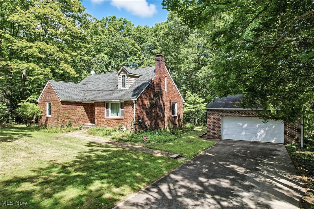 Cape cod-style house featuring a chimney, a front yard, brick siding, and a detached garage
