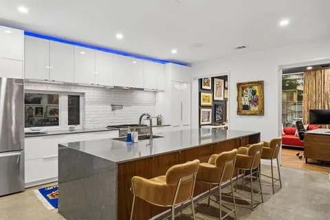 a kitchen with stainless steel appliances granite countertop a stove a sink a refrigerator white cabinets and couches with wooden floor