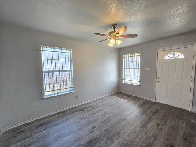 an empty room with wooden floor chandelier fan and windows