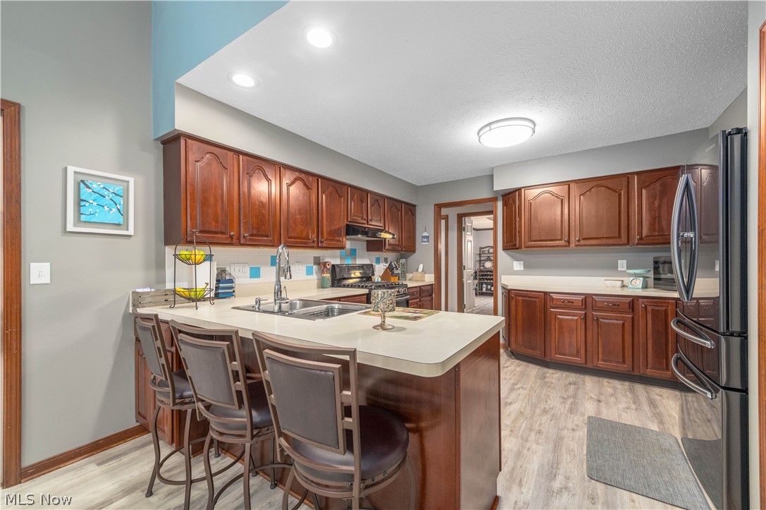 44565 Stang Road Elyria, OH 44035 - Photo 12 of 50 Kitchen with a breakfast bar, stainless steel appliances, a peninsula, light countertops, and waterproof vinyl plank floors
