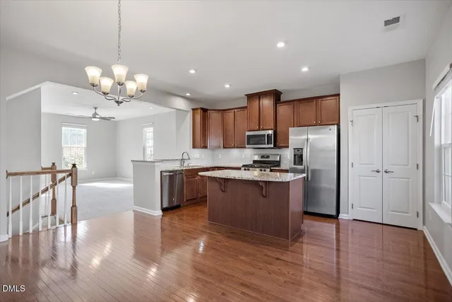 a large kitchen with granite countertop a large center island a sink dishwasher a stove and a refrigerator with wooden floor