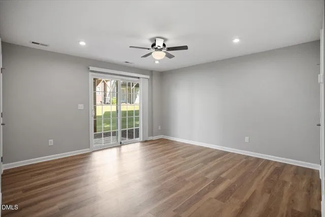 an empty room with wooden floor ceiling fan and windows