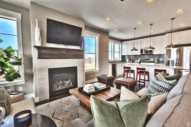 252 East Sandy Sage Way Sandy, UT 84070 - Photo 12 of 36 Living area featuring a gas fireplace with a wood mantel, tile surround, and a kitchen with white cabinetry, stainless steel appliances, and a central island with bar seating