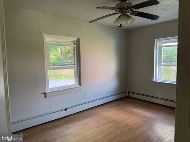 an empty room with wooden floor chandelier fan and windows