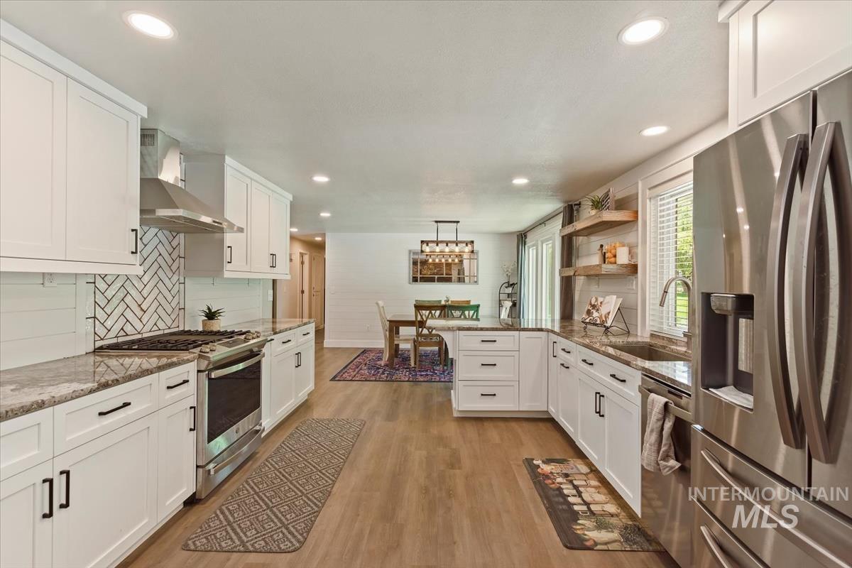 13712 Jarett Street Caldwell, ID 83607 - Photo 15 of 39 Kitchen featuring white cabinetry, appliances with stainless steel finishes, hanging light fixtures, light stone countertops, and wall chimney range hood