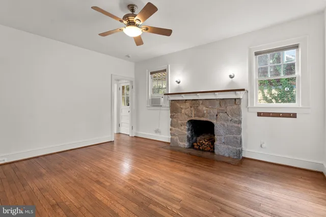 a view of a livingroom with a fireplace a ceiling fan and brick wall clock